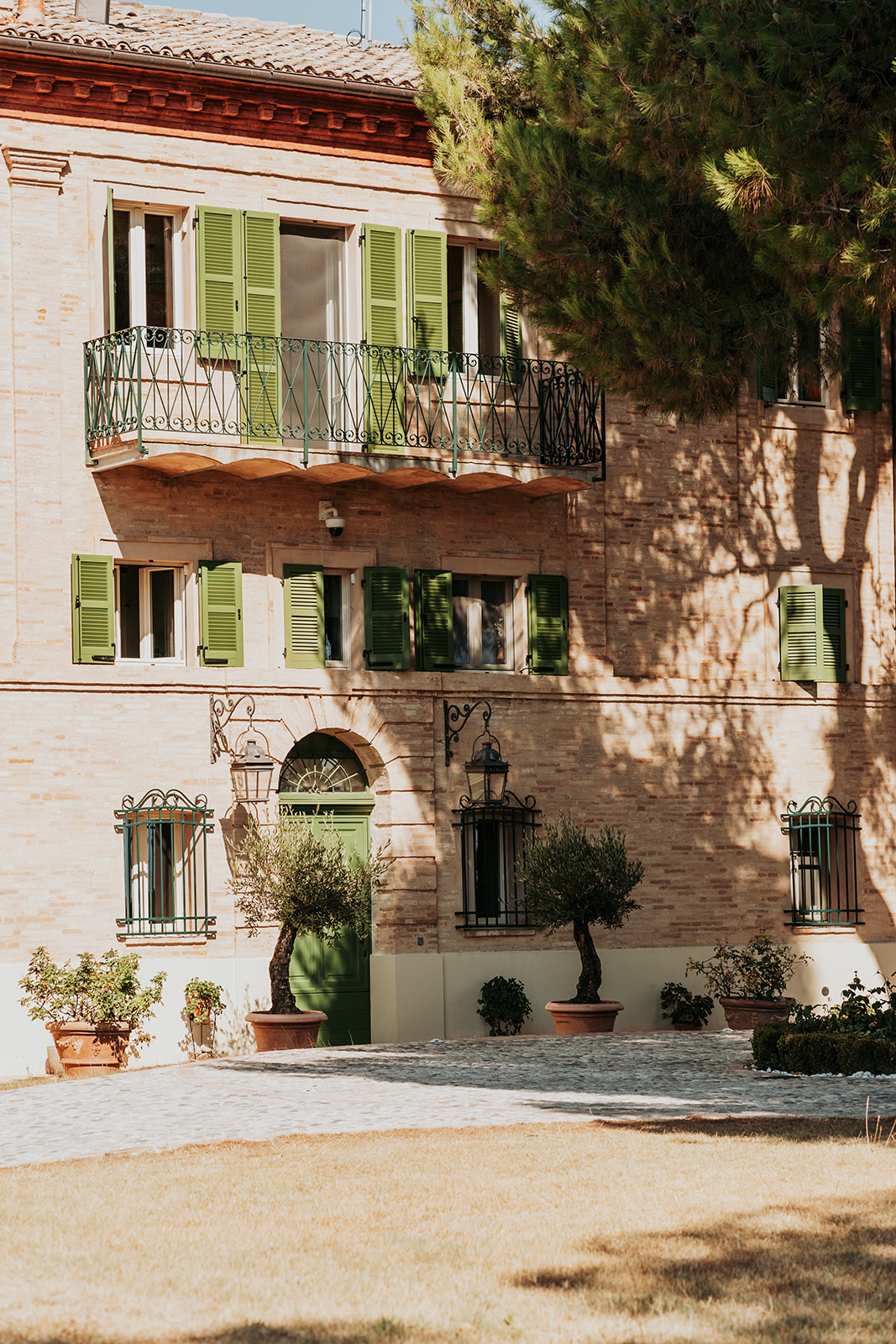 Maniero Montecassiano manor facade with dappled afternoon light and green shutters, Le Marche Italy