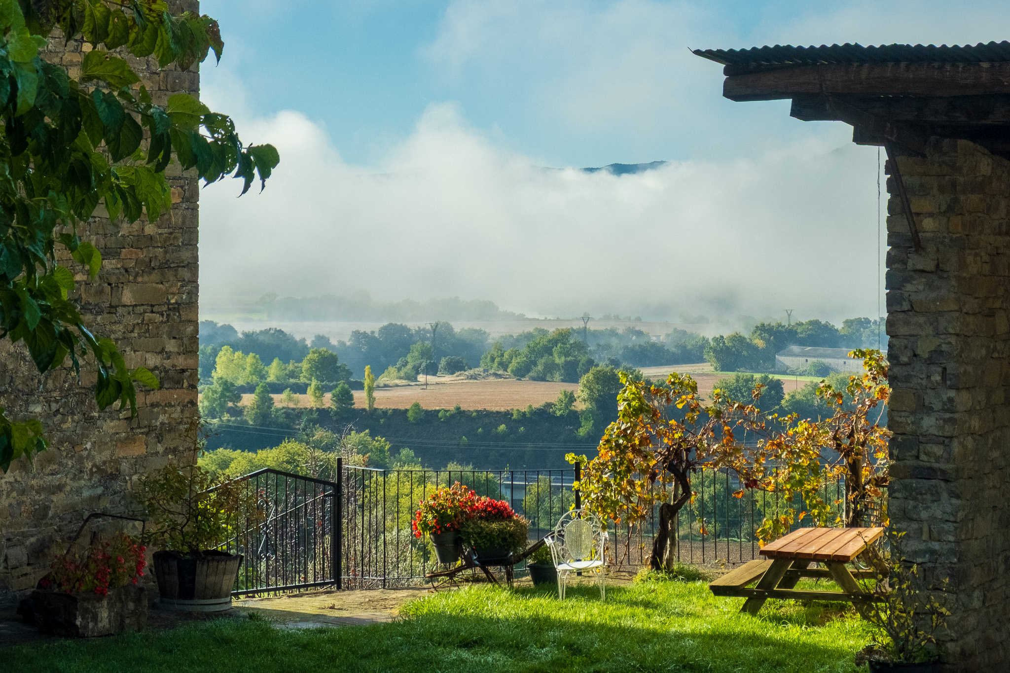 Morning mist over rolling Mediterranean landscape, framed through ancient stone walls