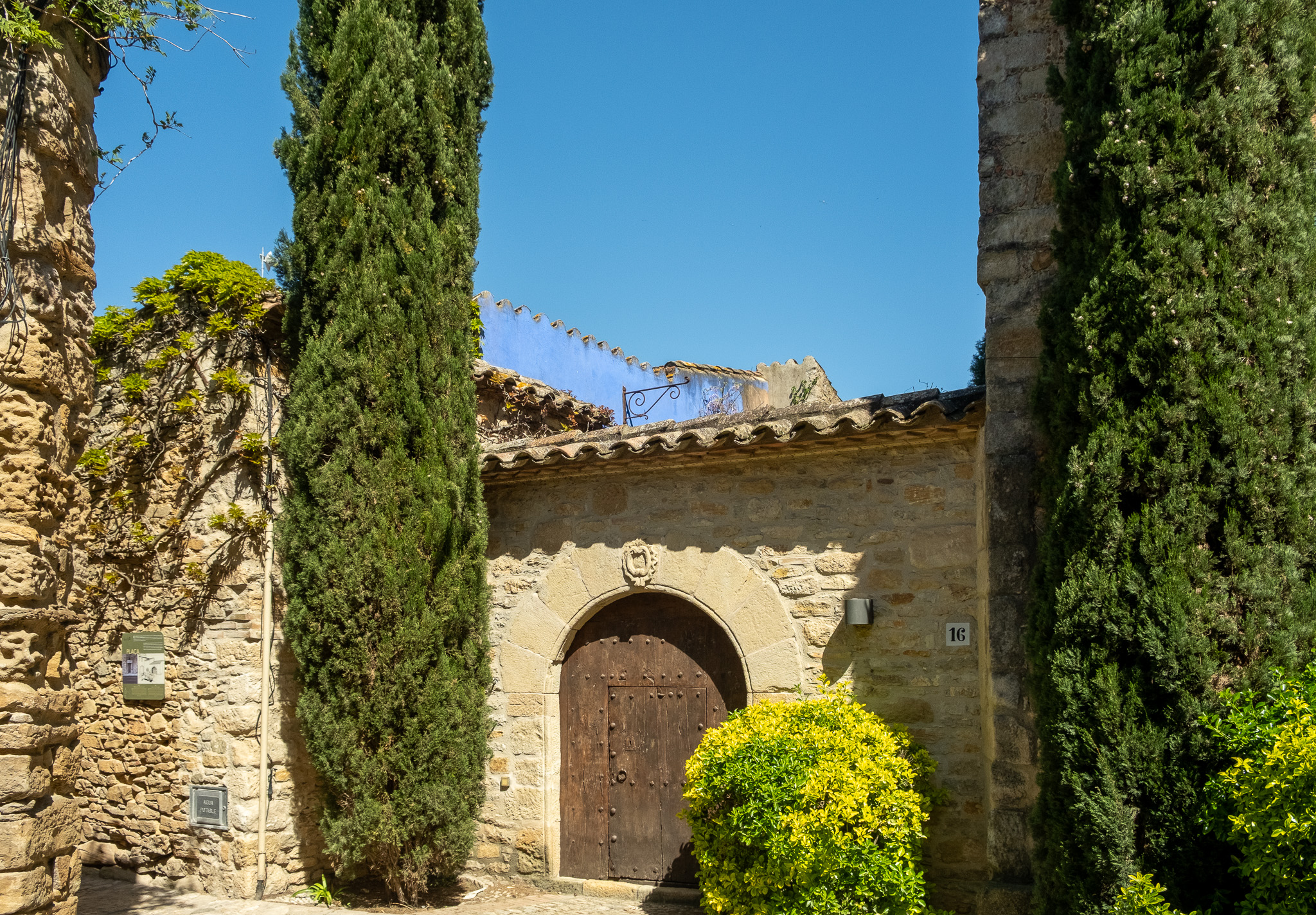 Ancient stone gateway flanked by cypress trees under a clear Mediterranean sky
