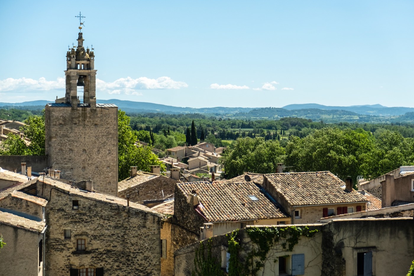 Provence village rooftops with bell tower and rolling hills in Mediterranean summer light